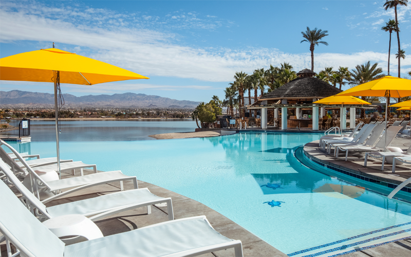 The infinity pool and palapa bar surrounded by lounge chairs and sun umbrellas with a view of Lake Havasu.