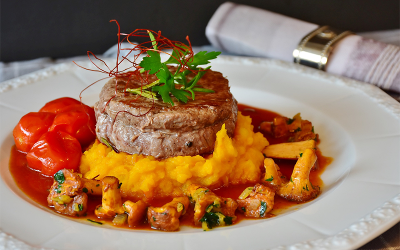 A filet mingnon on a bed of mashed sweet potatoes garnished with grilled cauliflower and tomatoes